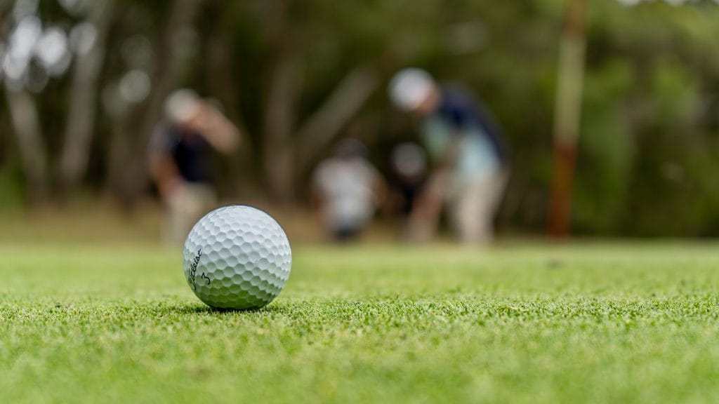 Golf ball on the green with a group of friends playing pitch and putt Vancouver style in the background